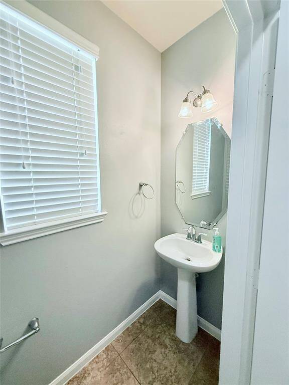 Chic half bathroom featuring a modern pedestal sink, elegant lighting, and a bright window for natural light.