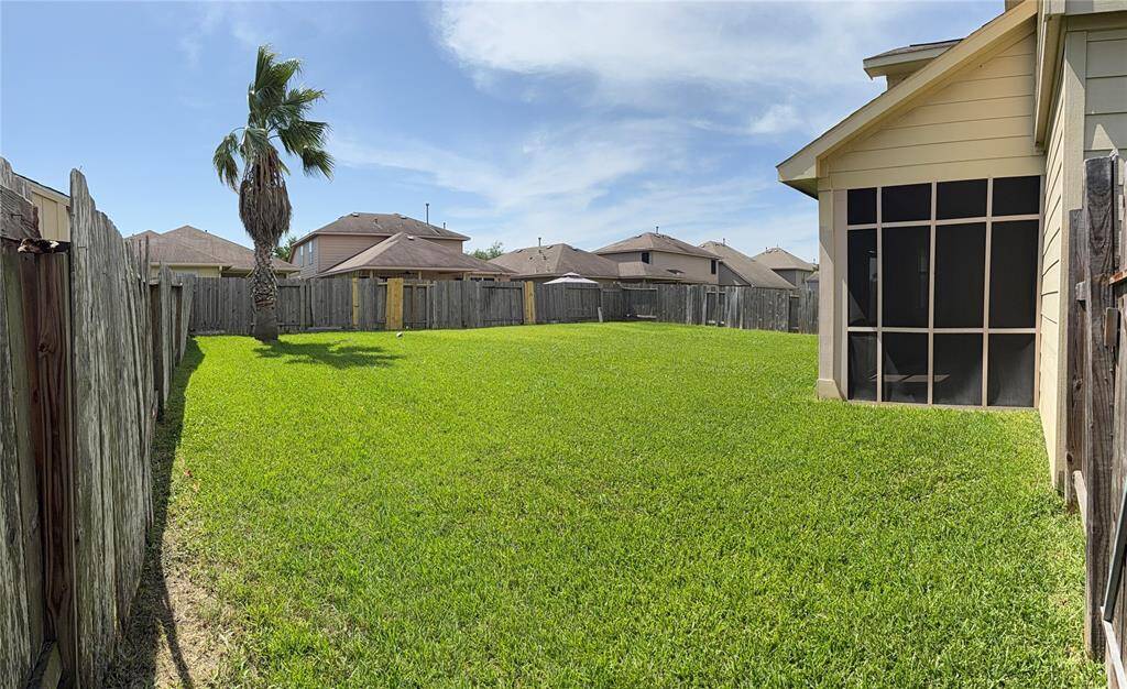 Spacious backyard with a well-maintained lawn, surrounded by a wooden fence for privacy. Features a screened patio area and a single palm tree, ideal for outdoor relaxation.