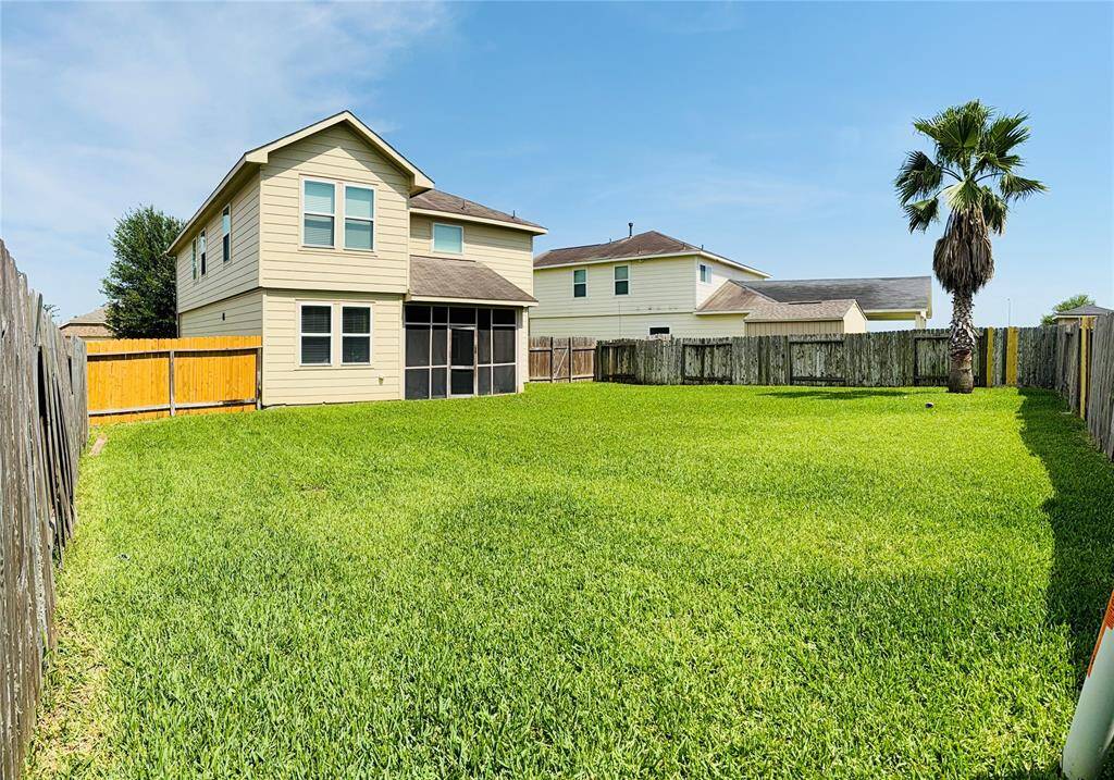 A spacious, fenced backyard with a well-maintained lawn. The two-story house features a light exterior and screened-in patio, perfect for outdoor enjoyment.