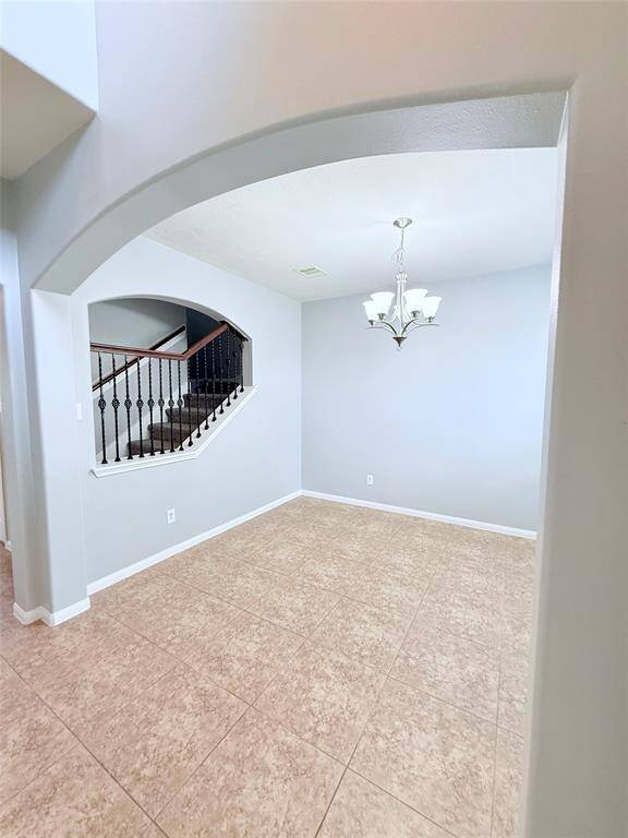 Elegant dining area with a charming chandelier, tile flooring, and an open archway view to the staircase, perfect for entertaining.