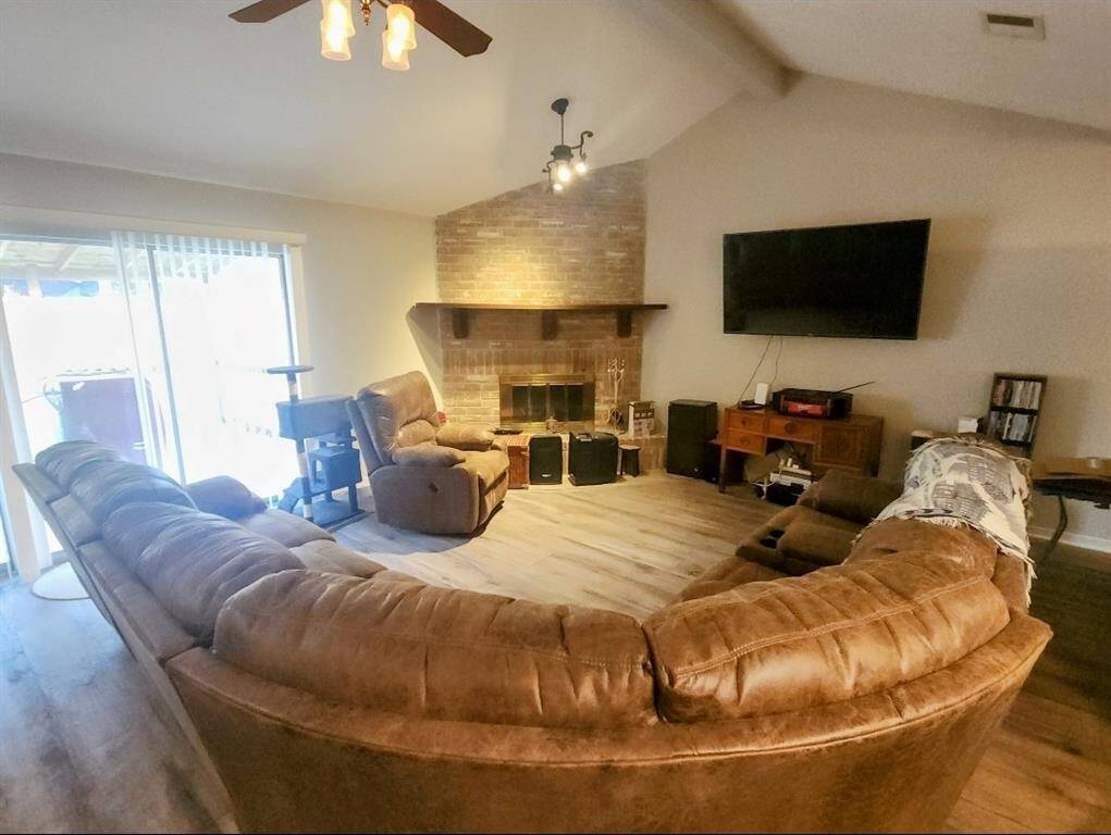 Cozy living room with a vaulted ceiling and brick fireplace. Sliding glass doors provide ample natural light and access to the outside.