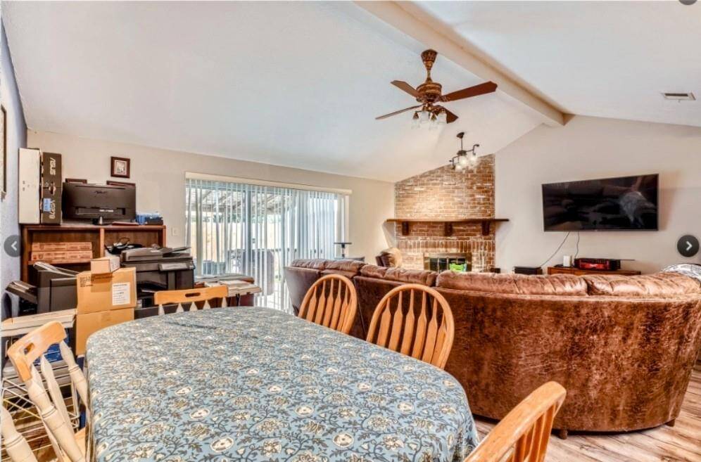 This spacious living area features a high ceiling with a fan, a cozy brick fireplace.  Sliding glass doors provide access to the outdoor space, adding natural light.