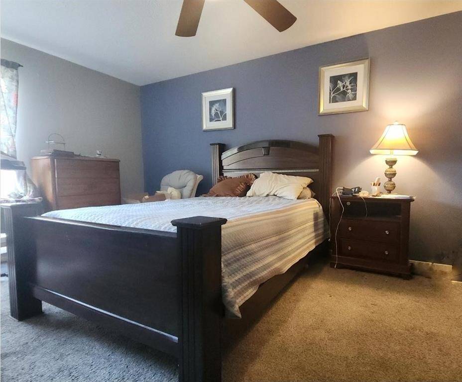 Cozy bedroom with  soft carpeting. Features a soothing color palette, ceiling fan, and warm lightiing Ideal for relaxation.