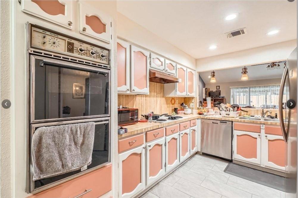 This kitchen features retro-style cabinets , a double oven, and a stainless steel dishwasher. The space is well-lit with recessed lighting and has a cozy, vintage charm.