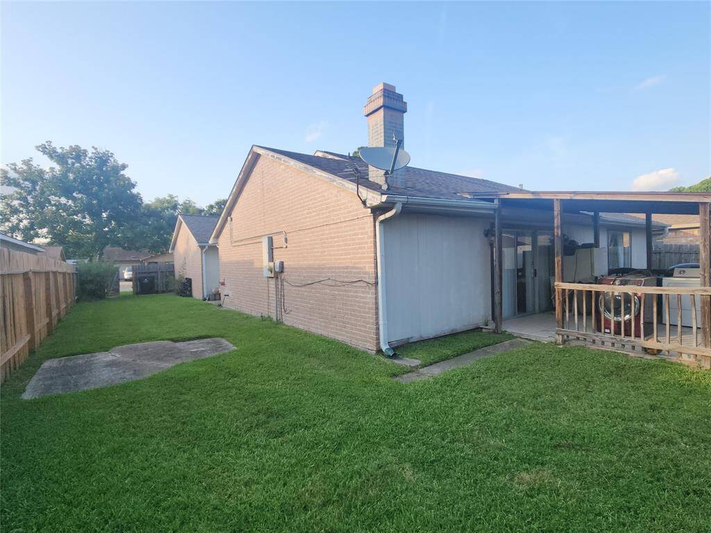 single-story brick home with a fenced backyard. There's a covered patio area and a small concrete slab, suitable for outdoor activities. The yard is grassy and well-maintained, offering a cozy outdoor space.