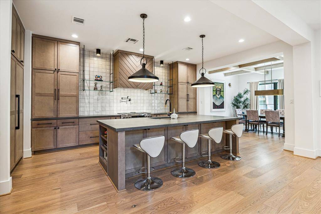 Kitchen has sleek white tile backsplashes, built-in paneled refrigerator and quartz countertop.