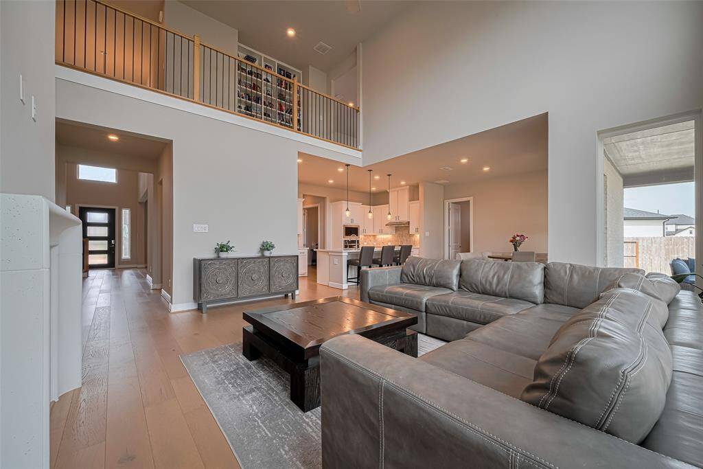 This spacious living area features a high ceiling and an open concept design, connecting seamlessly with the modern kitchen. It includes ample natural light from large windows and an upstairs overlook.