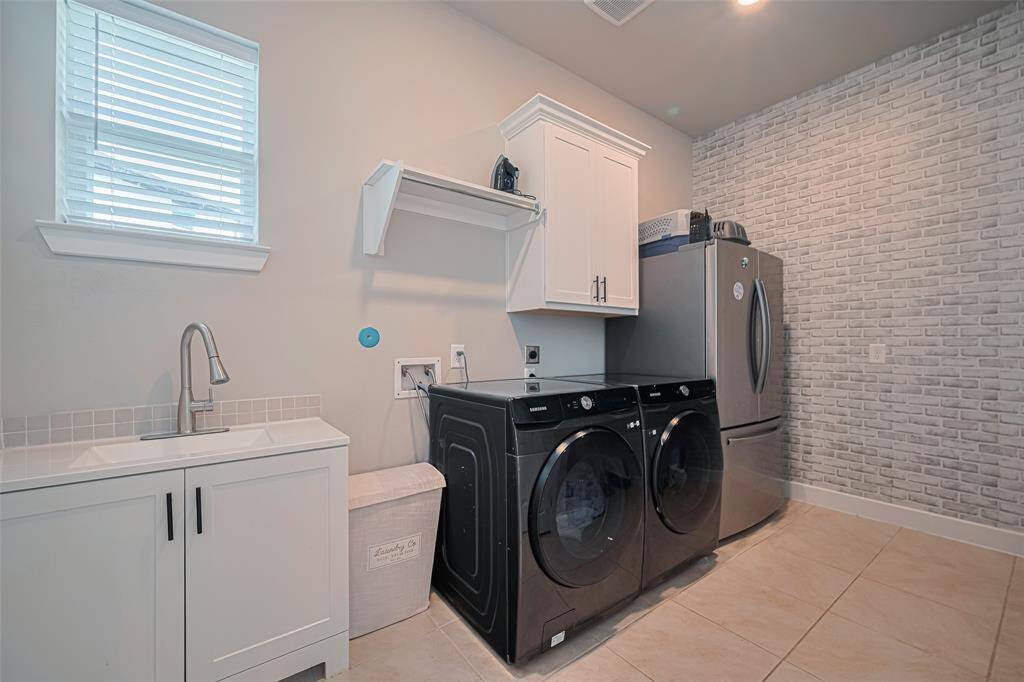 A large laundry room has a utility sink with storage, room for a fridge and/or deep freeze and a stylish brick-patterned accent wall.