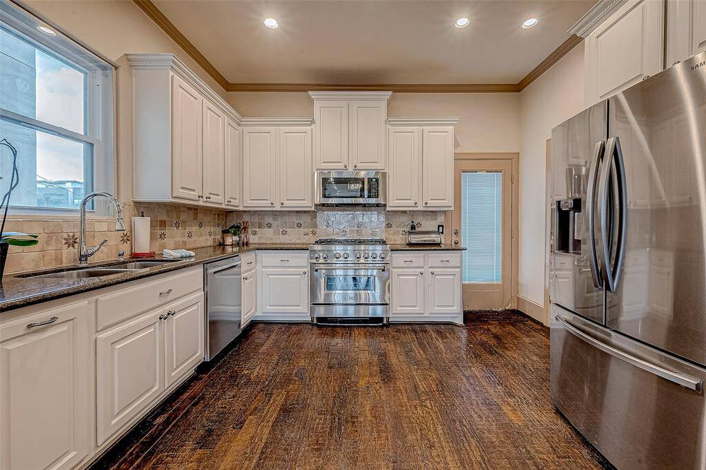 The kitchen boasts white cabinetry, stainless steel appliances, granite countertops, and dark wood floors, all with plenty of natural light