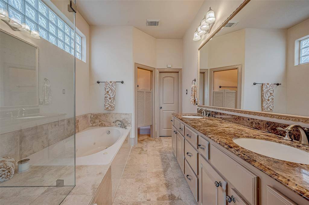 This spacious bathroom offers a luxurious bathtub, a large glass-enclosed shower, and a double vanity with granite countertops.