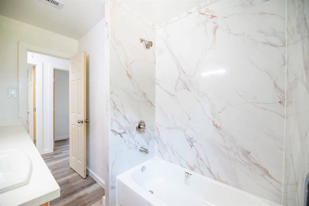 This bathroom features a clean, modern design with a white marble-look tiled shower and bathtub. It has a bright interior with light wood flooring and a sleek vanity.