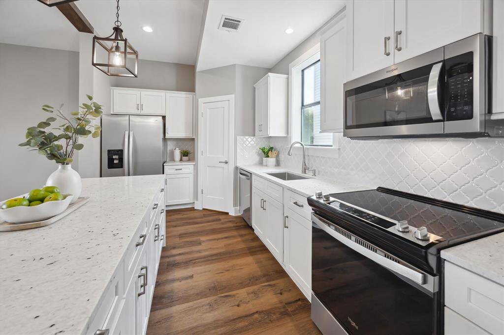 Outfitted with stainless steel Whirlpool appliances, this kitchen combines function and flair—complete with a decorative tile backsplash, quartz counters, and abundant cabinetry to keep everything beautifully organized.