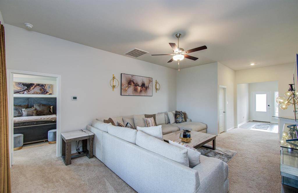 This cozy living room easily fits a large L-shaped sofa and showcases neutral tones and a ceiling fan.