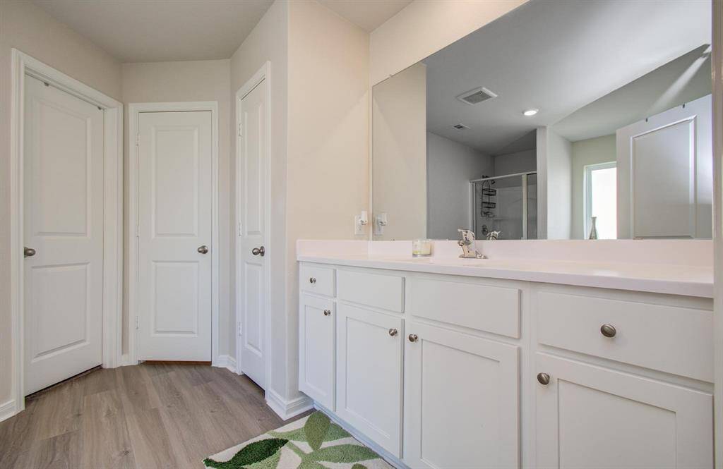 Bright and spacious bathroom featuring a large mirror, white cabinetry, and a modern shower. The room has a clean, minimalist design with ample storage and sleek fixtures.