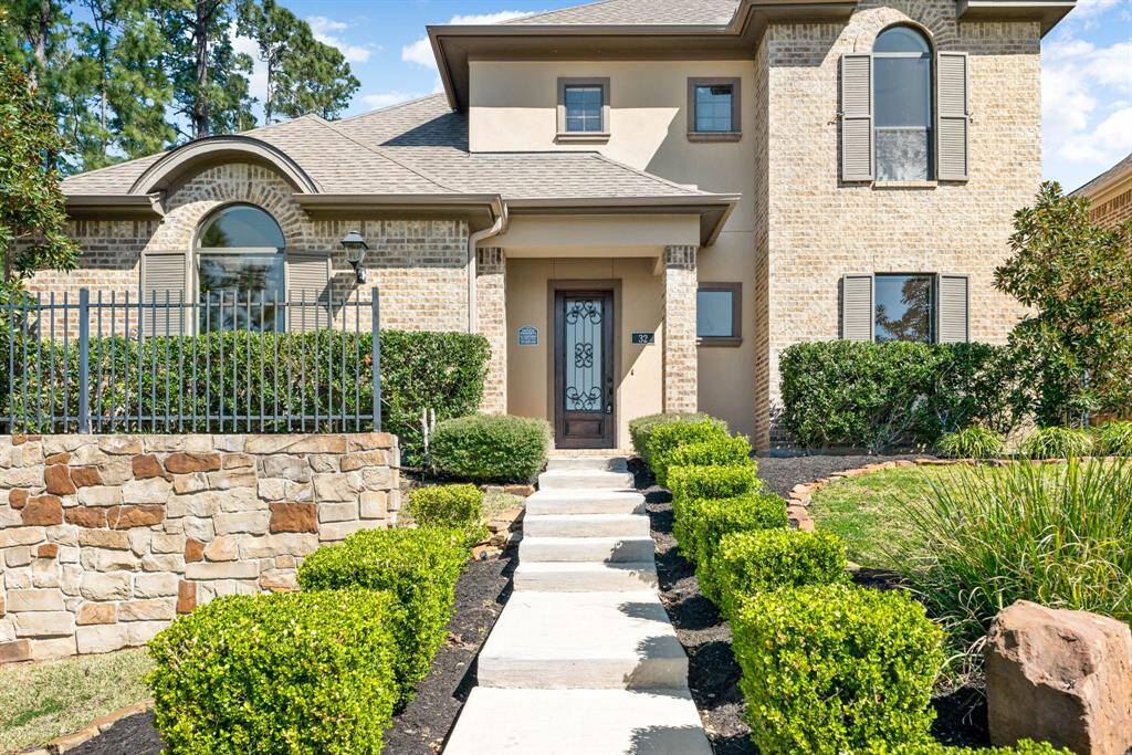 This beautiful two-story home features arched windows and decorative shutters. A manicured pathway, lined with hedges, leads to a welcoming front entrance.