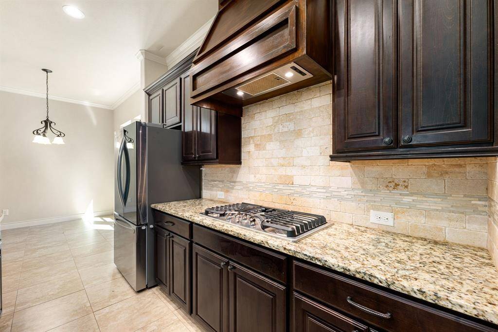 This kitchen features dark wood cabinetry, a granite countertop, and a stylish tile backsplash. It includes a gas cooktop and stainless-steel refrigerator
