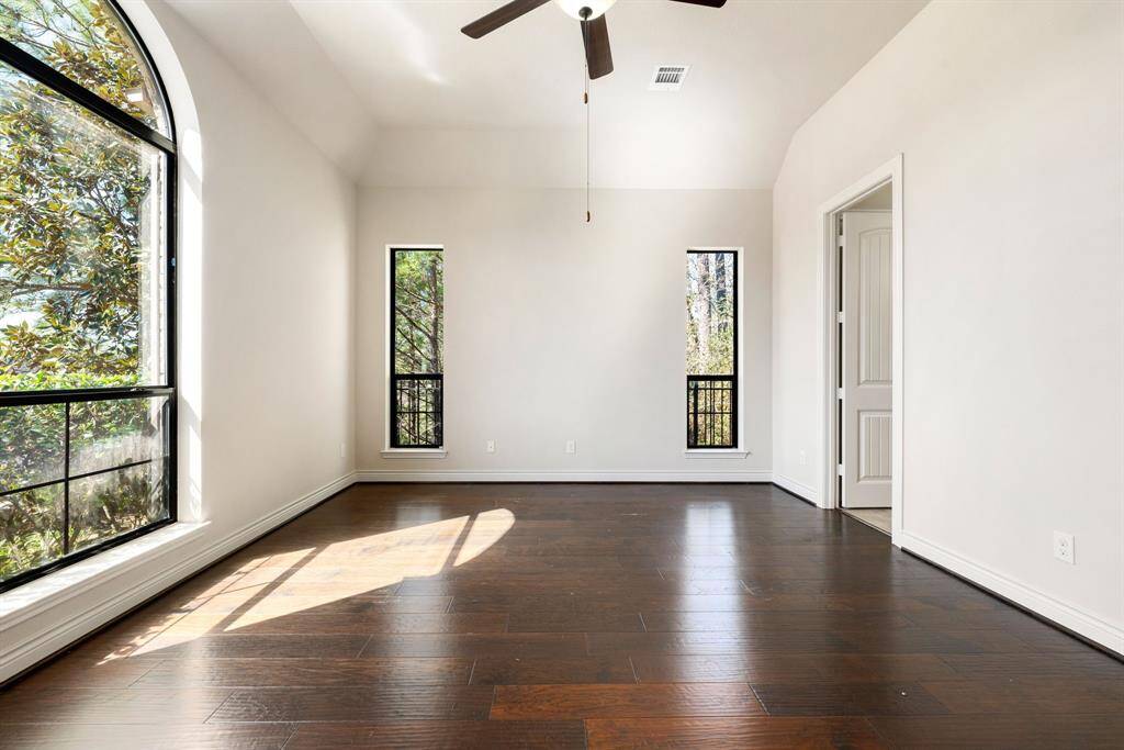 The Primary room features large windows with natural light, a high ceiling with a fan, and rich hardwood flooring, creating a welcoming and airy atmosphere.