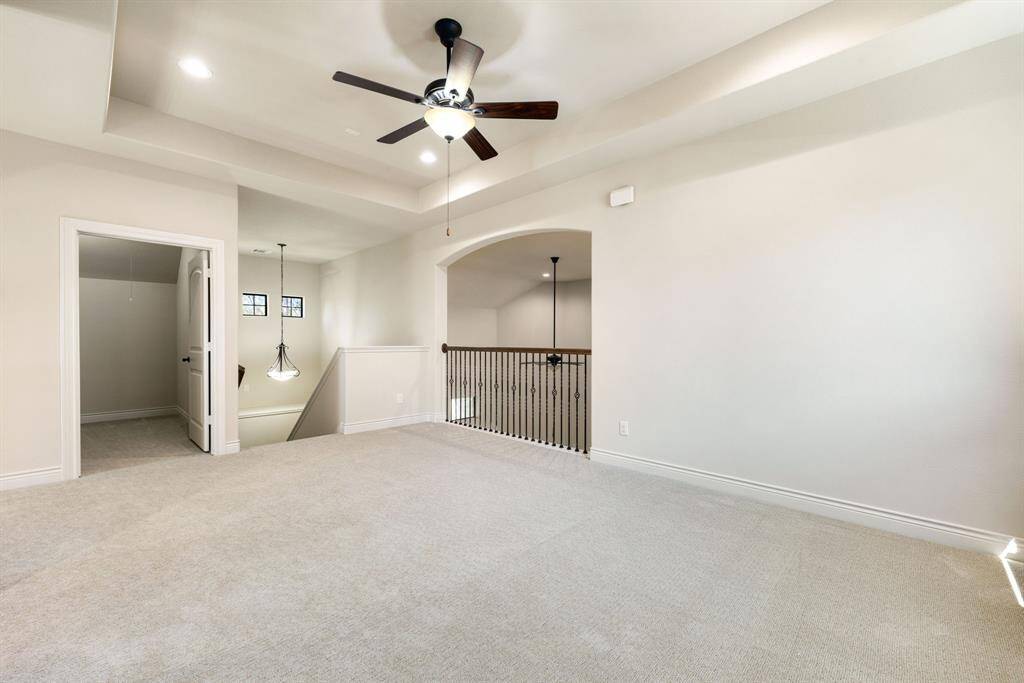 This spacious gameroom features a ceiling fan, recessed lighting, and an open railing overlooking the living room. It has neutral walls and a doorway leading to an adjacent room, providing a versatile space for various uses.