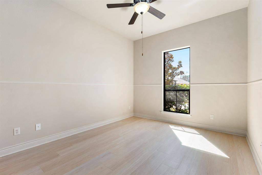 Another secondary bedroom located downstairs that features light wood flooring, a ceiling fan, and a large window that lets in natural light, creating a warm and inviting atmosphere. This room also has its own ensuite bathroom.