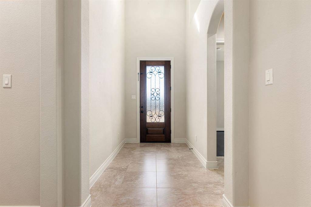 This photo showcases a bright, welcoming entryway with high ceilings, neutral walls, and elegant tile flooring. The front door features decorative glass, creating a stylish first impression.