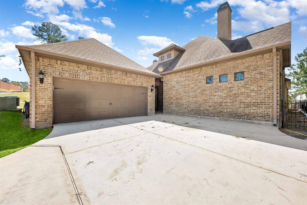 A spacious driveway leading to a large two-car garage. The house features a pitched roof and decorative exterior lighting, surrounded by a well-maintained lawn and trees, offering a welcoming entrance.