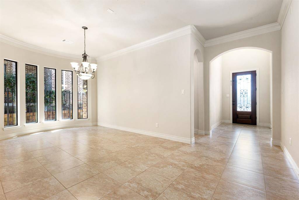 This spacious dining room features large windows for ample natural light, elegant tile flooring, and a stylish chandelier. The neutral walls and crown molding provide a sophisticated touch