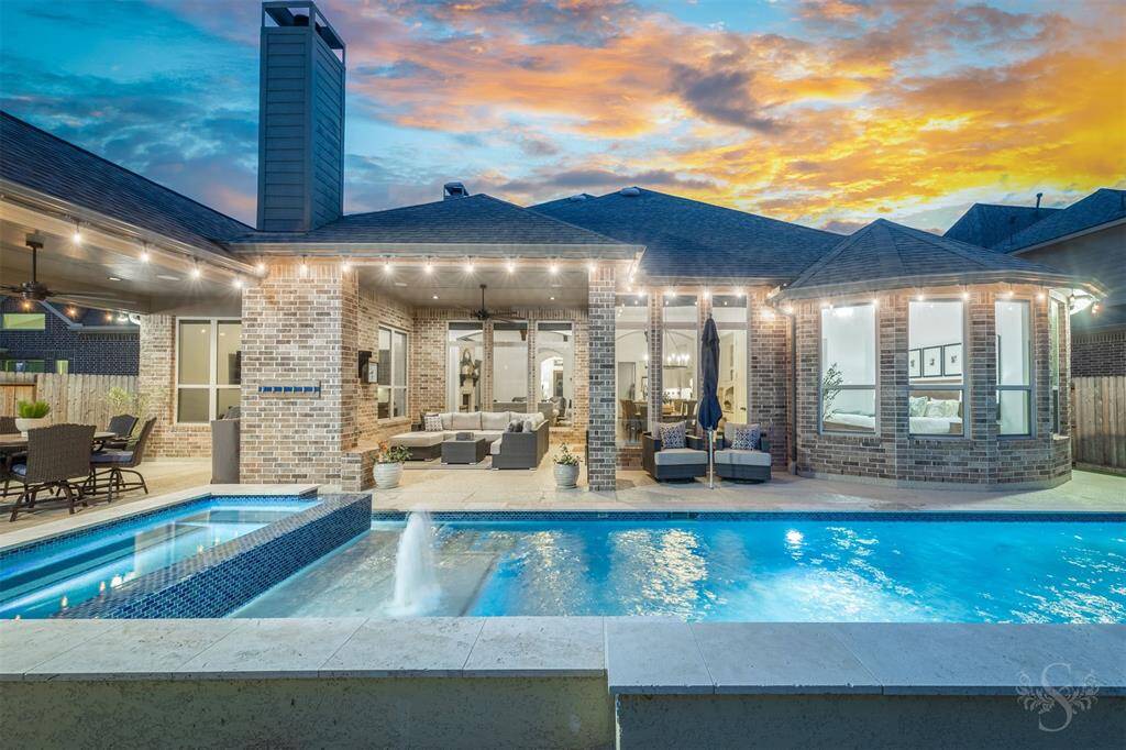 This stunning home features a spacious outdoor area with a pool and spa, perfect for entertaining. The brick exterior, large windows, and covered patio with seating create a welcoming atmosphere. Enjoy beautiful sunset views and modern outdoor living.
