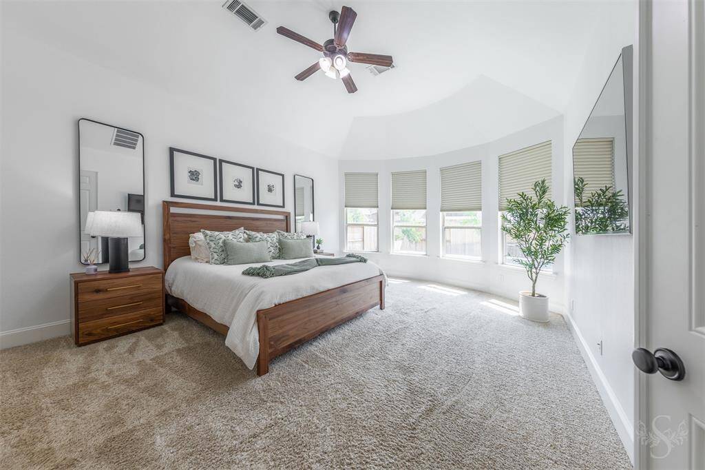 The spacious primary bedroom features plush carpet, high ceiling, a ceiling fan and ample natural light from several windows with blinds. A cozy ambiance makes this a perfect space for relaxation.