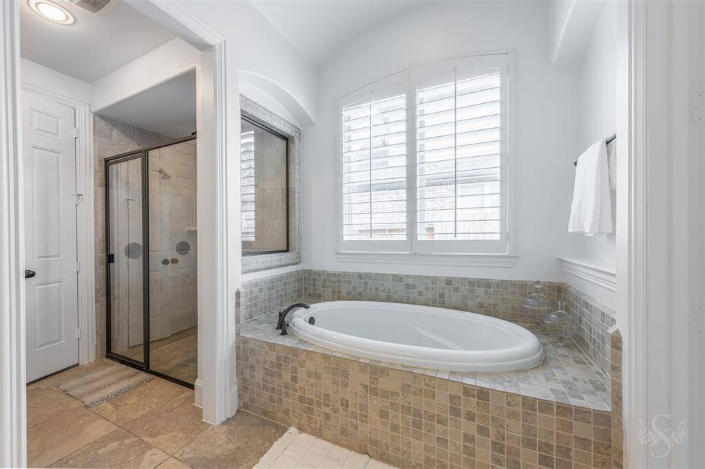 Custom tile adorns the massive bathtub with sitting ledge. Large window with white shutters.