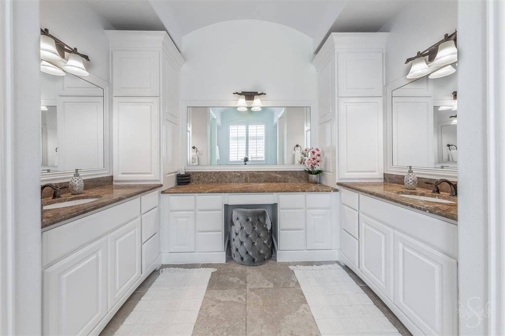 This spacious, elegant Primary bathroom featuring dual sinks with, stylish wall sconces, and a central vanity area with a mirror, perfect for daily routines.