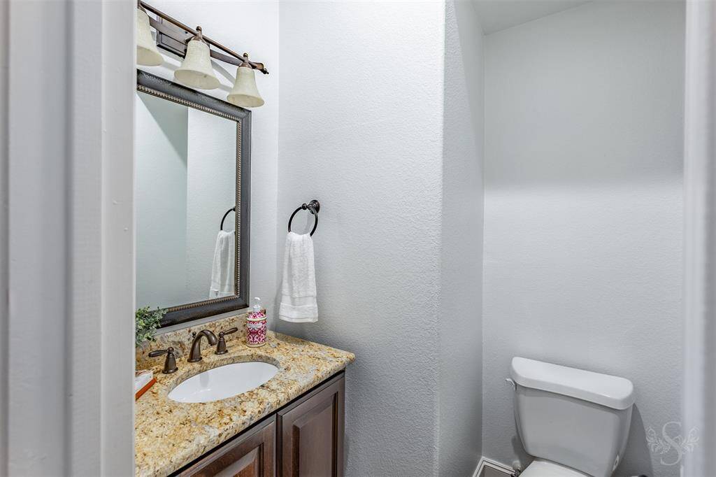 The powder room is conveniently located in a hallway, featuring a granite counter top and cabinet for additional storage.