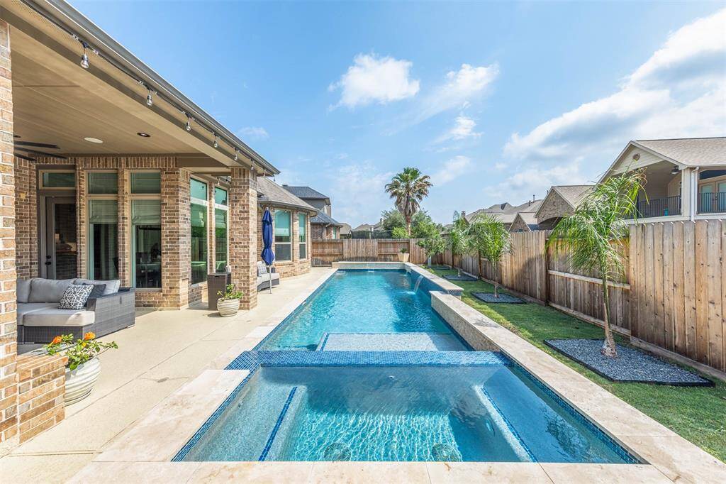 This photo showcases a luxurious backyard with a modern swimming pool and spa, surrounded by a landscaped patio and seating area. The space is private, with a wooden fence and tropical plants, perfect for relaxation and entertaining.