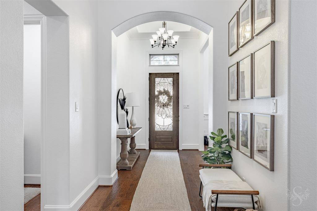 This inviting entryway features a stylish wooden door with decorative glass, a high ceiling with a chandelier, and elegant hardwood flooring.