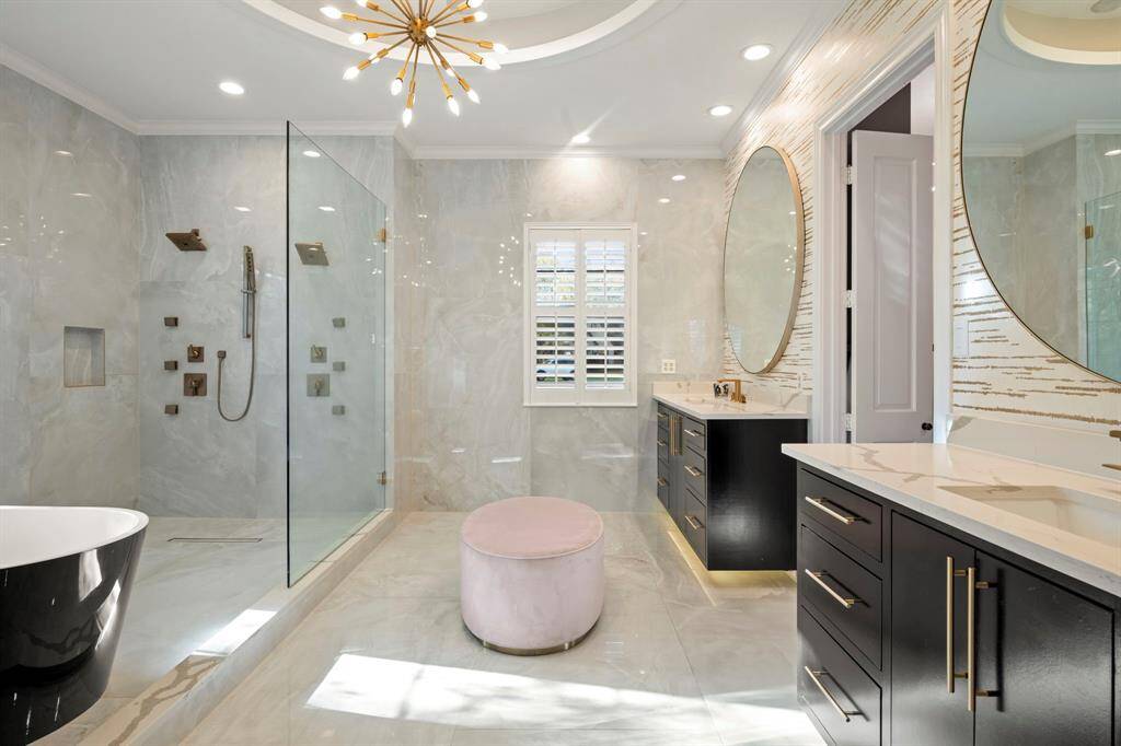 Hotel spa like primary bathroom featuring two sinks, custom vanity with accent floor lighting, TOTO toilet, soaking tub, designer ceiling light and wall paper