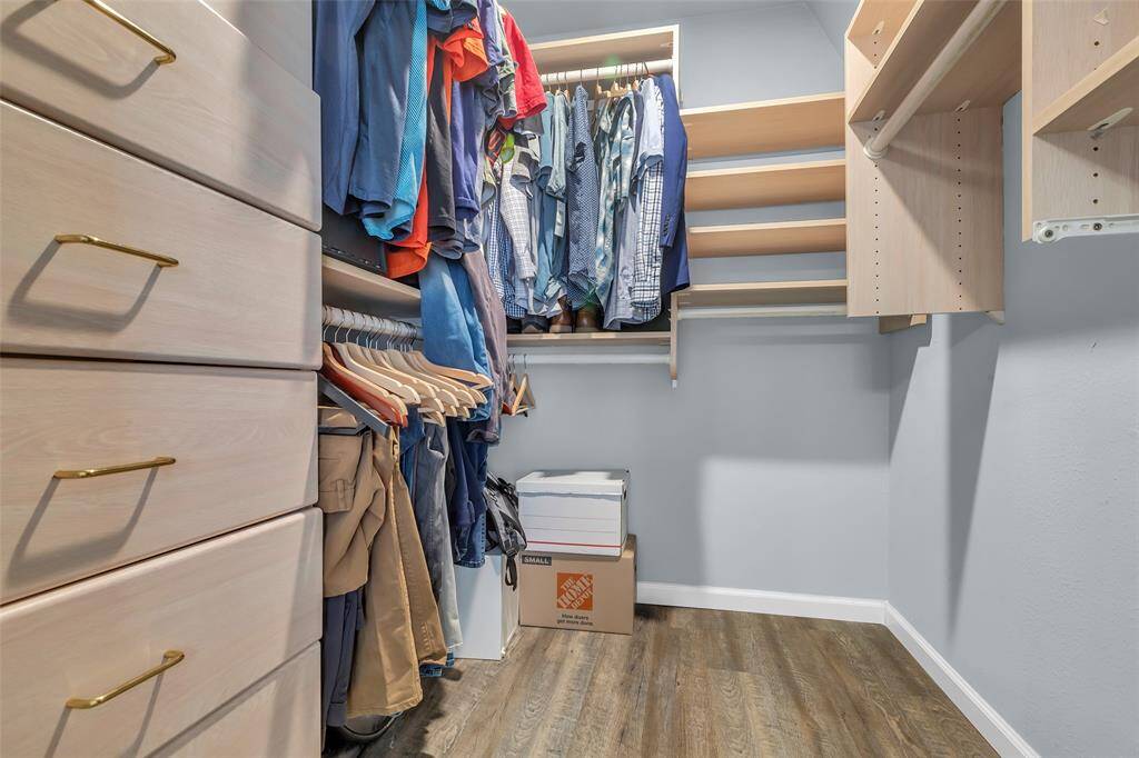 Upgraded walk-in closet with integrated drawers, gold hardware, adjustable shelving, and dual hanging rods. Designed for optimal storage and convenience, perfect for a fashion-forward homeowner.