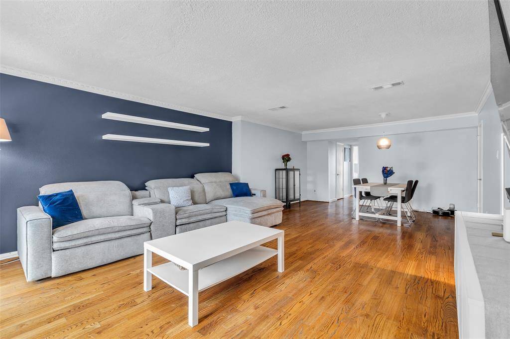 Spacious and bright open-concept living and dining area with updated hardwood flooring and crown molding. A bold navy accent wall adds modern sophistication, complemented by floating shelves and neutral tones throughout.