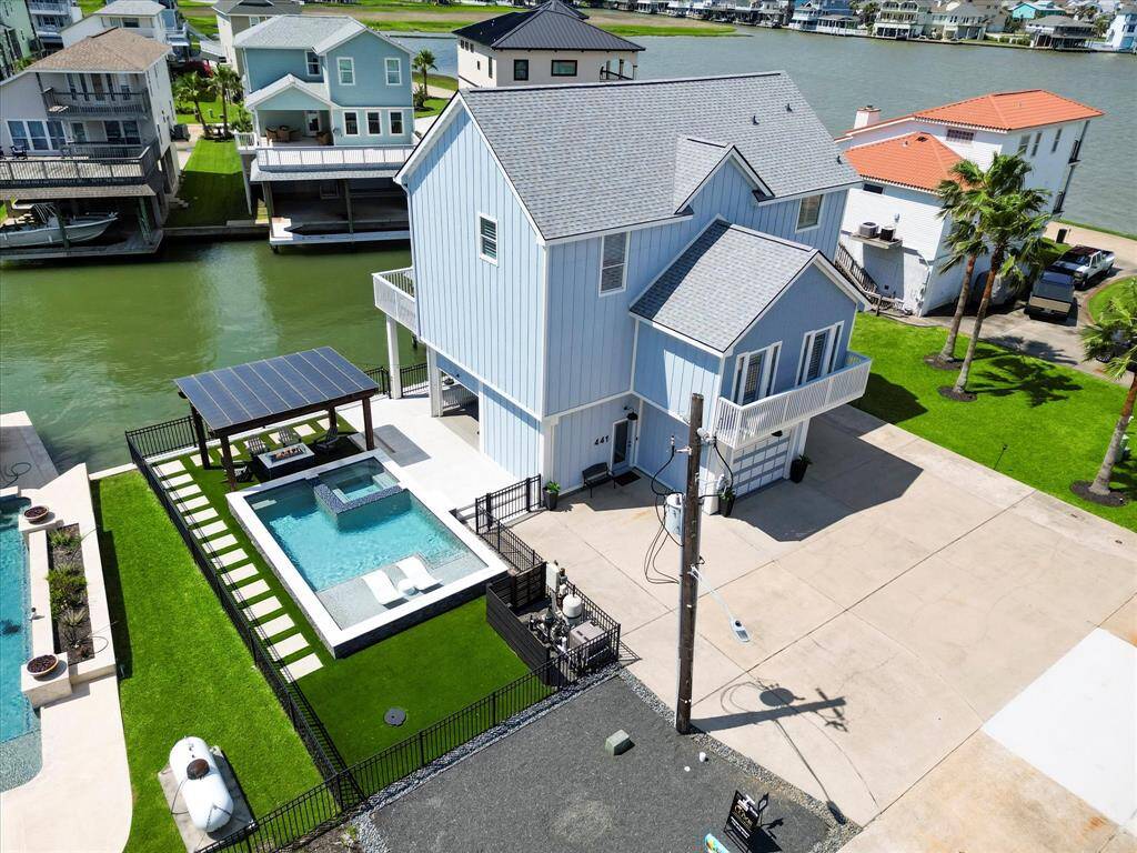 This waterfront home features a modern, multi-story design with a private pool and spa, a pergola-covered patio, and a spacious driveway. It's situated in a scenic neighborhood with direct water access, ideal for relaxation and entertaining.