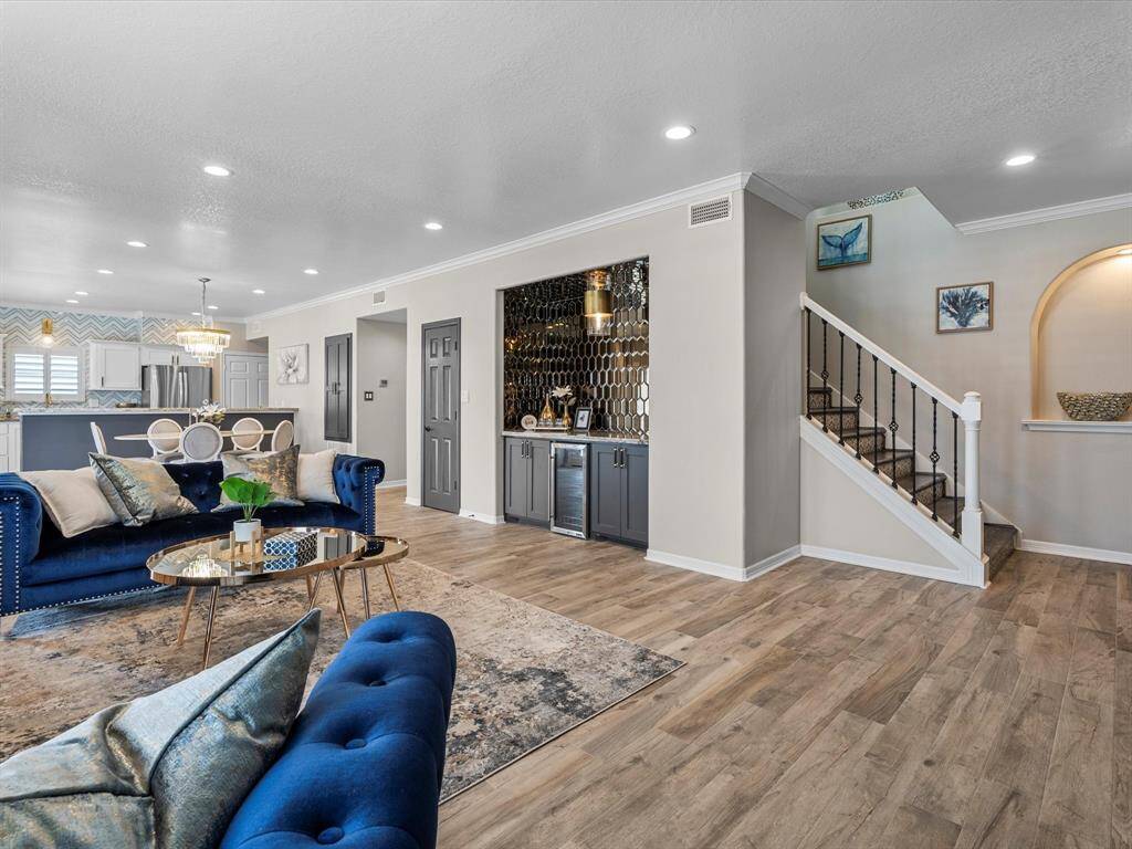This photo showcases a modern open-concept living area with stylish wood flooring, a cozy blue sofa, and a chic coffee table. The kitchen features elegant cabinetry and a breakfast bar. A staircase with wrought iron railings leads to the upper level, complemented by tasteful decor and warm lighting.
