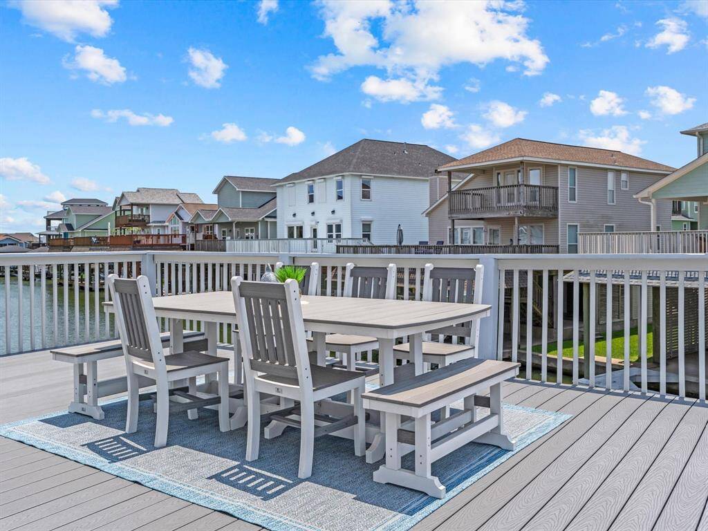 Spacious deck with modern outdoor dining set, overlooking a serene waterfront and neighboring homes, perfect for entertaining and enjoying the view.