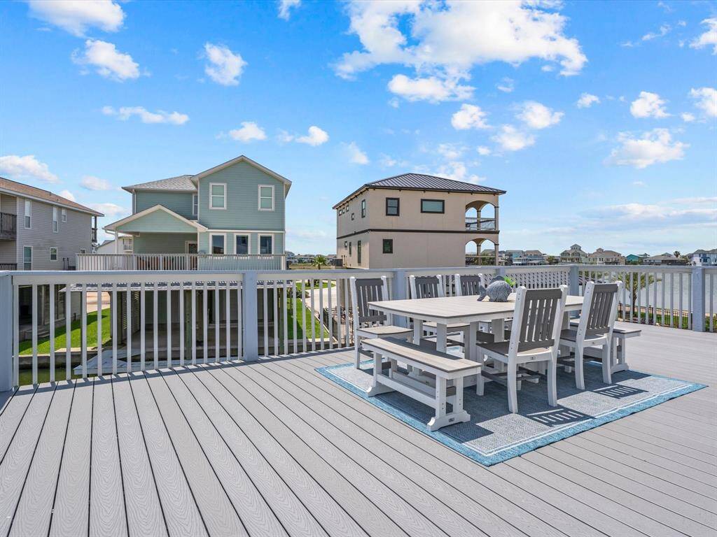 Spacious rooftop deck with outdoor dining set, offering scenic views of neighboring houses and a clear blue sky. Ideal for entertaining and relaxation.