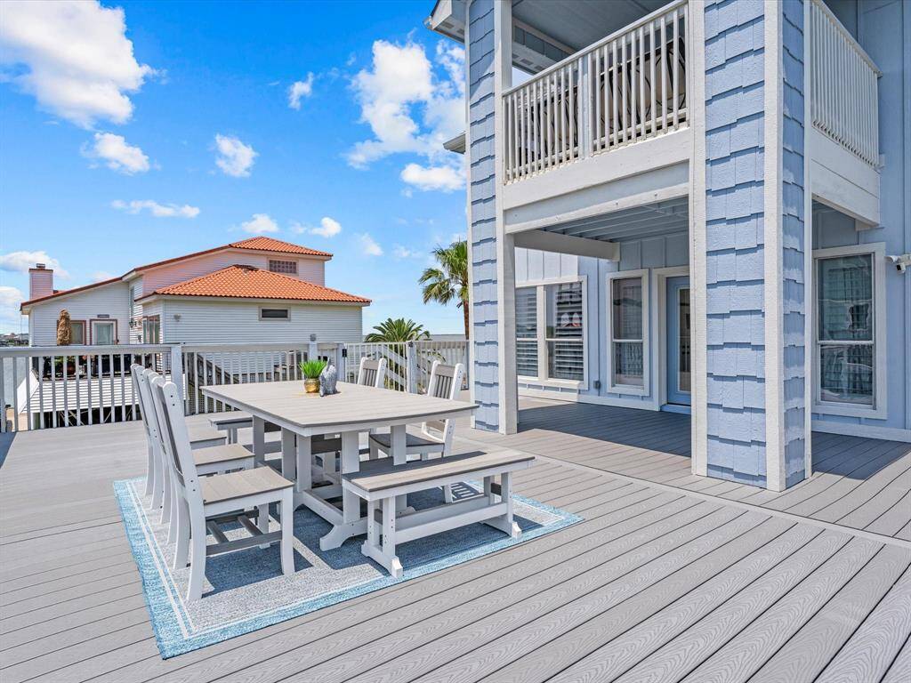 Spacious outdoor deck with modern, light gray furniture, ideal for entertaining. The area is open with a partial view of a neighboring home and clear blue skies, creating a bright and inviting atmosphere.
