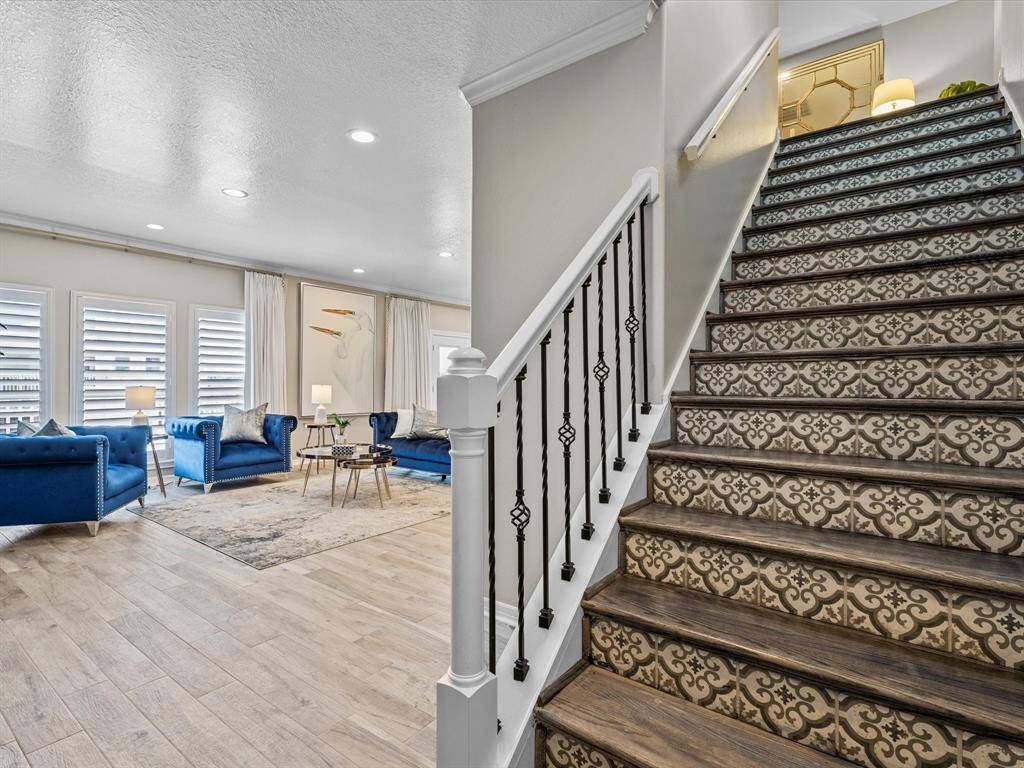 This inviting home features a stylish living area with blue sofas and ample natural light from large windows. The adjacent staircase has elegant patterned risers and a decorative railing, adding charm to the entryway.