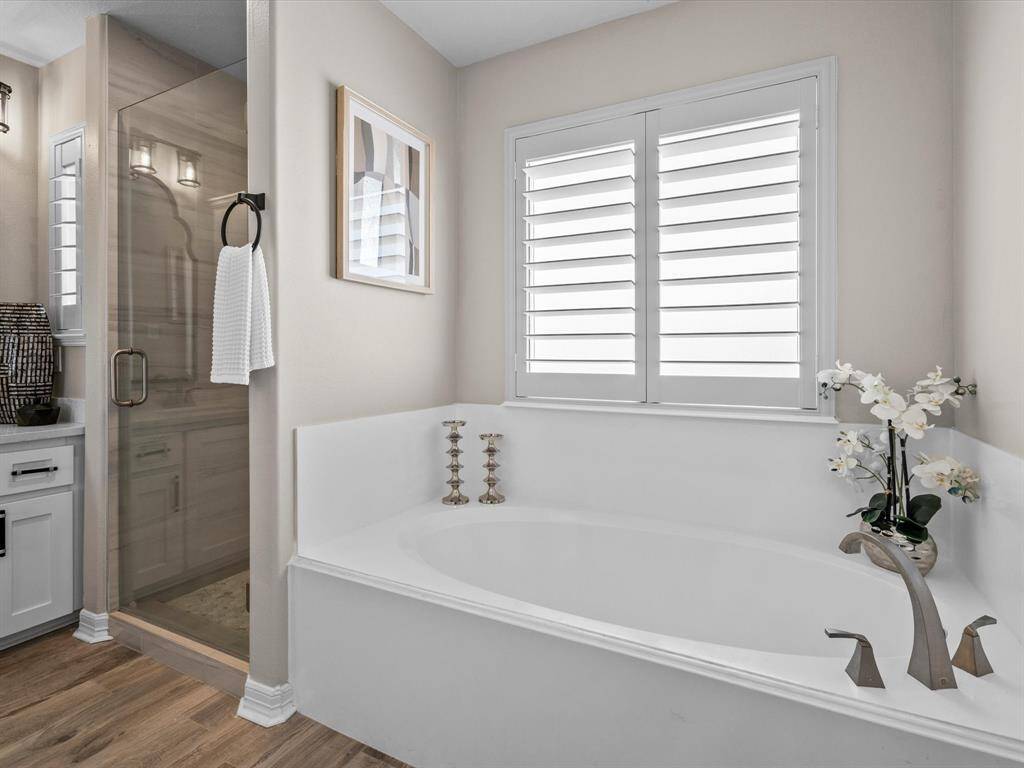 This bathroom features a modern design with a sleek glass-enclosed shower, a large soaking tub, and stylish fixtures. Natural light filters through window shutters, highlighting the neutral tones and elegant decor.
