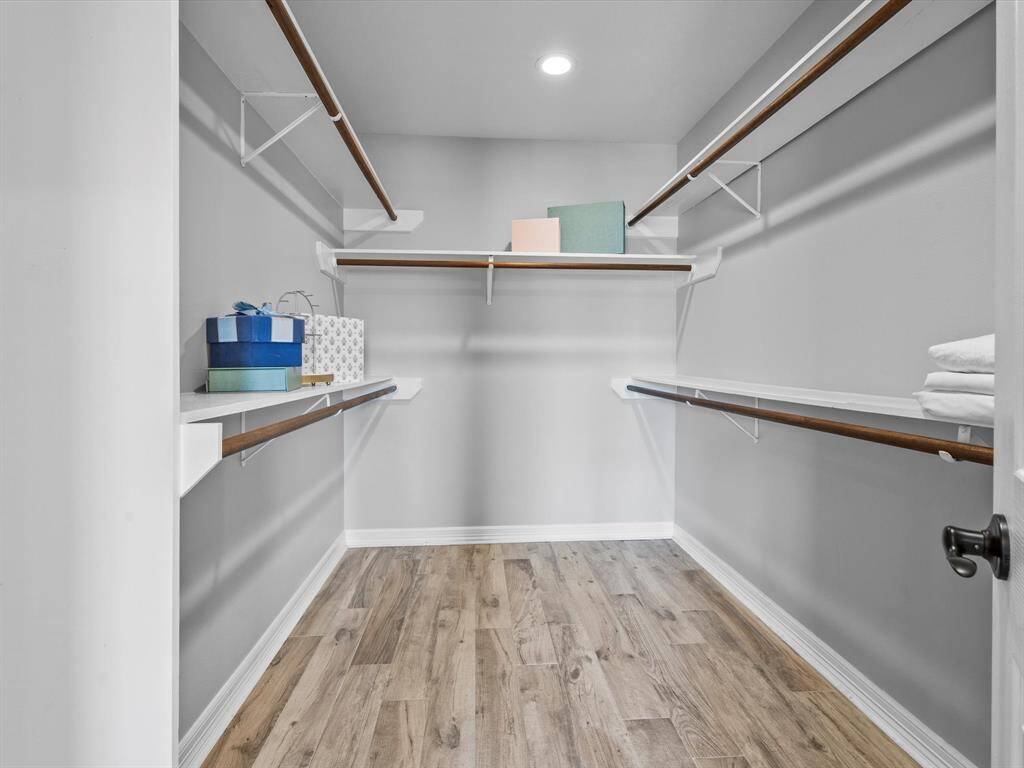 Spacious walk-in closet featuring wooden floors, ample shelving, and hanging space, ideal for organized storage.