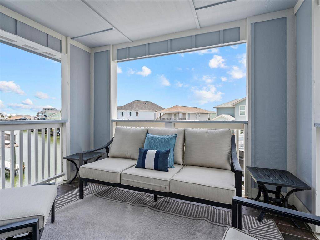 This photo showcases a cozy, covered outdoor seating area with comfortable furniture, surrounded by a railing. It offers a scenic view of neighboring houses and a waterway, providing a tranquil and inviting space to relax and enjoy the outdoors.