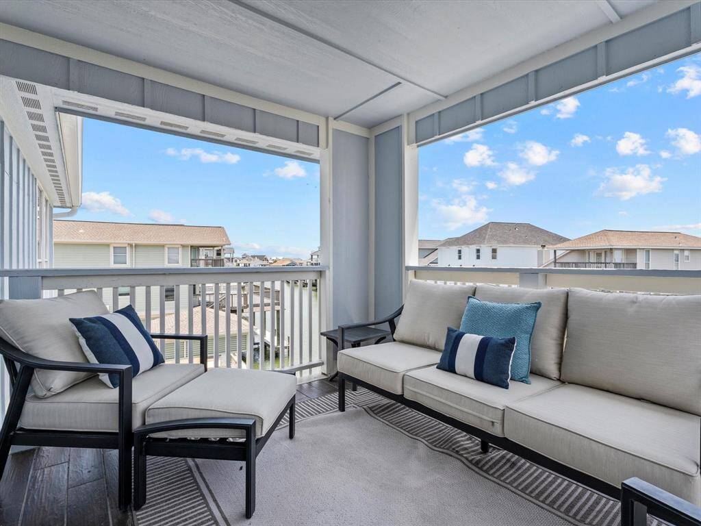 This photo showcases a cozy, covered balcony with comfortable seating, perfect for relaxation. It offers a pleasant view of nearby rooftops and a clear blue sky, ideal for enjoying outdoor moments.