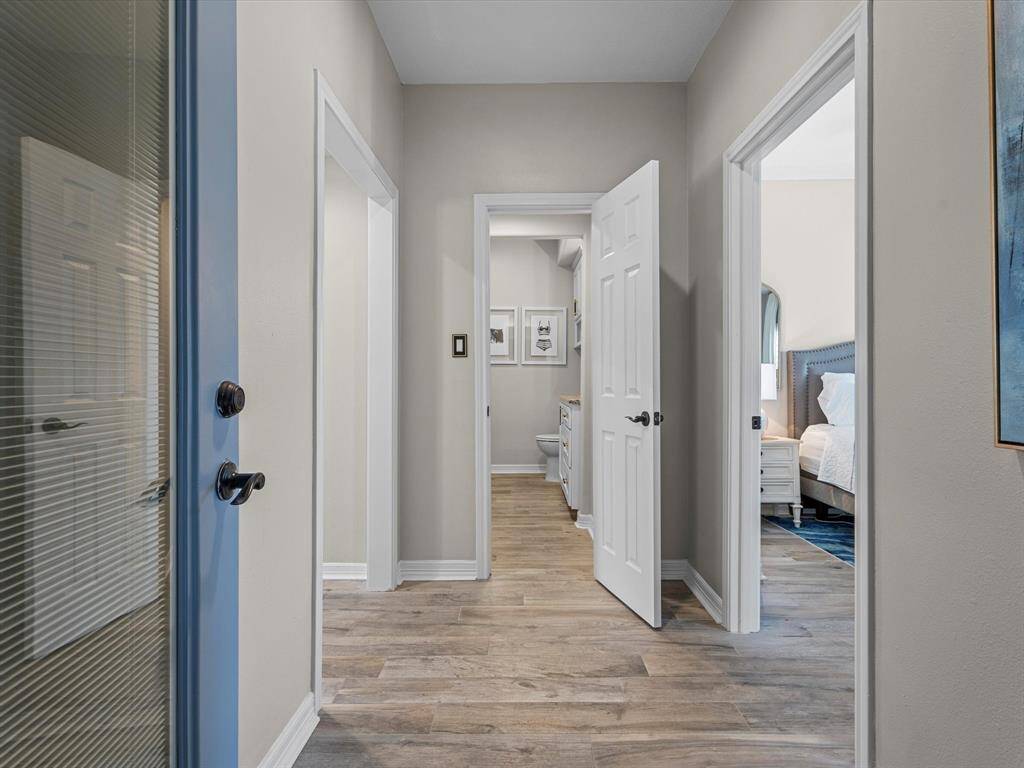 This photo shows a bright hallway with light wood flooring and neutral walls, featuring multiple doors leading to different rooms. The space feels inviting and well-lit, with glimpses of a bedroom and bathroom.