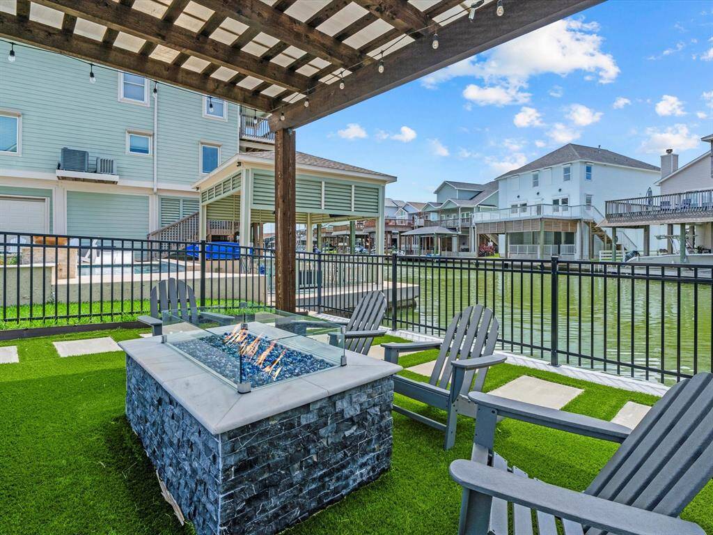 This outdoor space features a cozy fire pit with Adirondack chairs under a wooden pergola, overlooking a serene waterfront, perfect for relaxing and entertaining.
