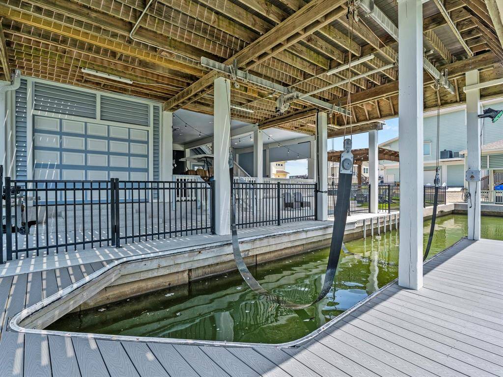 This photo showcases a covered boat dock with a lift system, surrounded by a fenced area and adjacent to a modern building. Ideal for waterfront living, it offers convenient access to water activities and secure storage for boats.