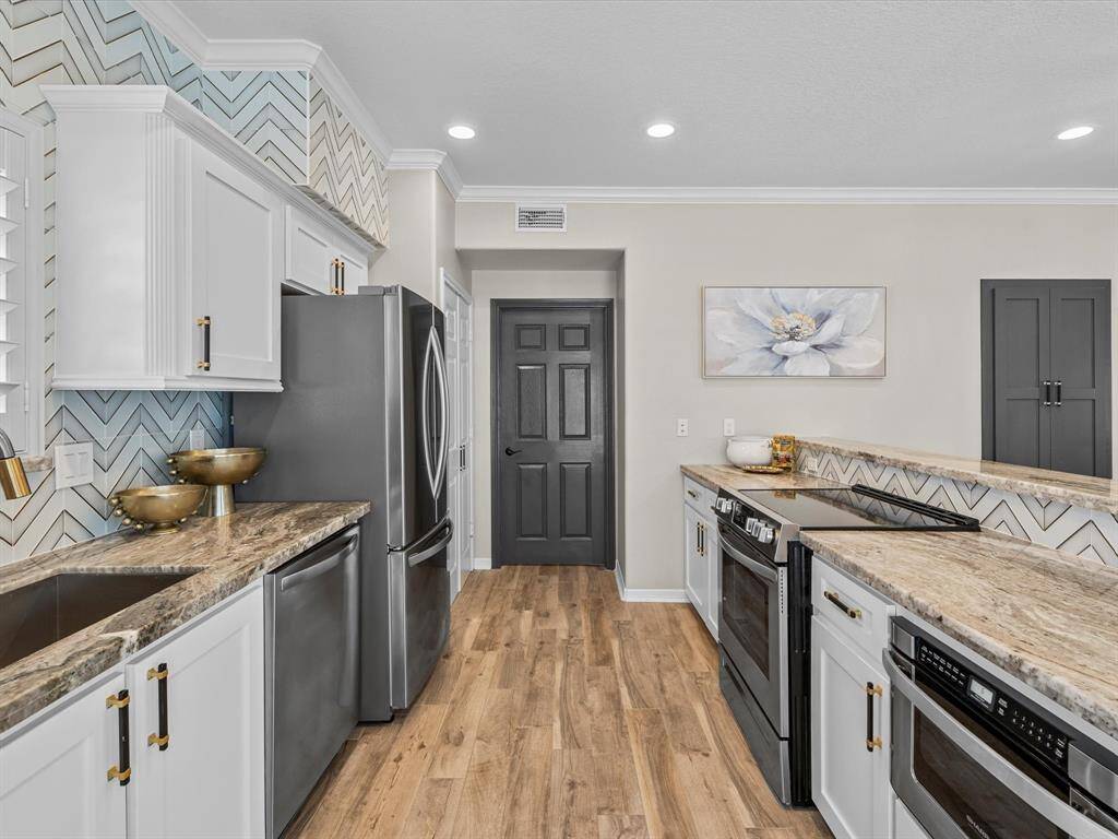 This kitchen features modern appliances, white cabinetry with gold hardware, and a stylish herringbone backsplash. It has granite countertops and wood flooring, creating a warm and inviting atmosphere.
